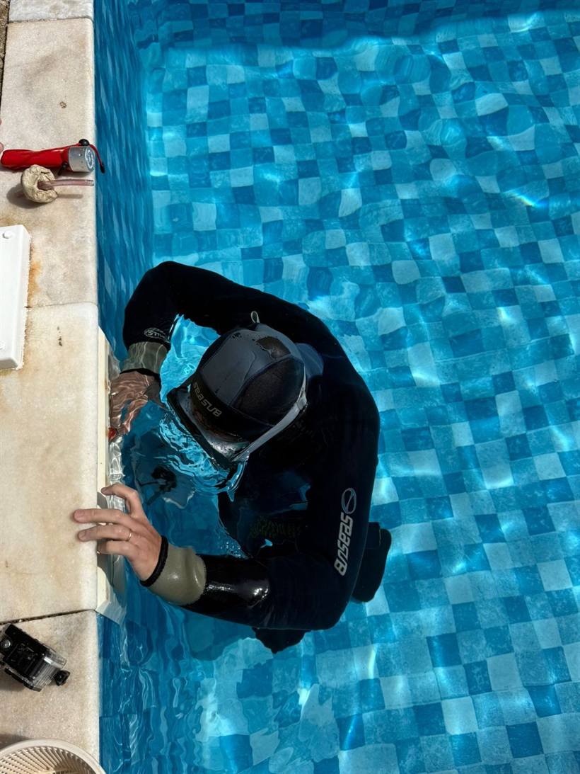 Profissional de roupa de neoprene analisando a parede da piscina junto a um dispositivo